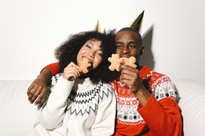 A couple in holiday sweaters taking a bite of gingerbread cookies for Christmas card photo ideas