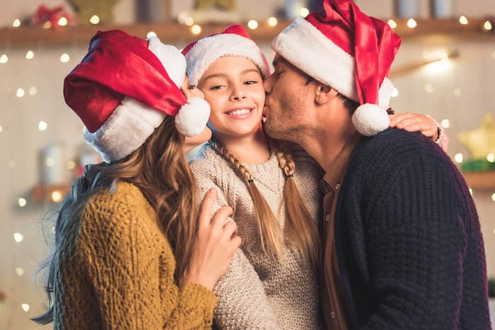 Child getting kissed by parents in Santa hats for Christmas card photo ideas