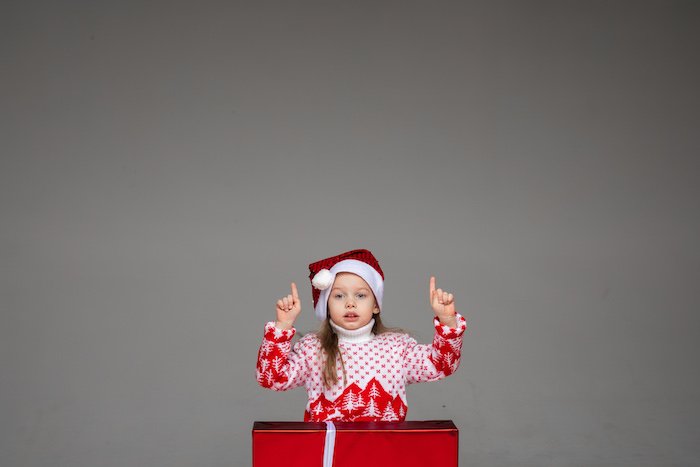 A kid wearing a Santa hat and holiday sweater as a present for Christmas card photo ideas