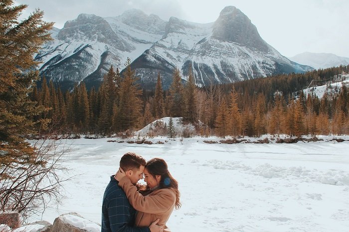 Christmas couple photoshoot ideas: a couple embraces in front of a snow capped mountain 