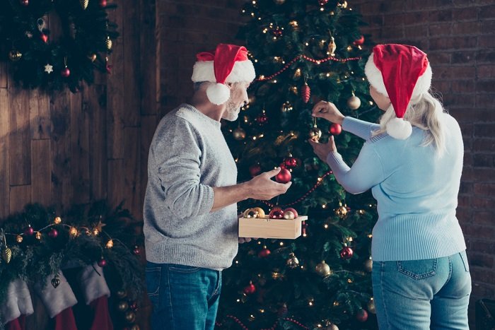 Christmas couple photoshoot ideas: a couple hanging red and gold Christmas bulbs on the tree