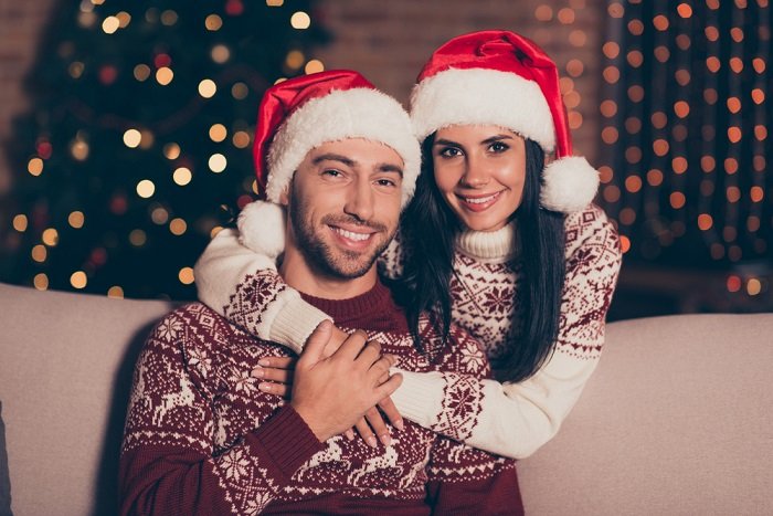 a portrait of a couple in Christmas sweaters and Santa hats