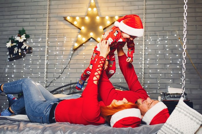 Tips for Christmas couple photoshoot: a couple laying on the bed holding up their child in his pajamas