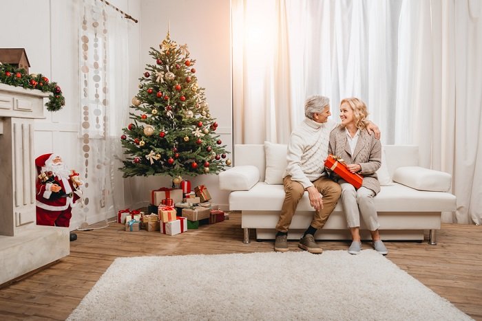 a portrait of a couple sitting on the couch next to their Christmas tree