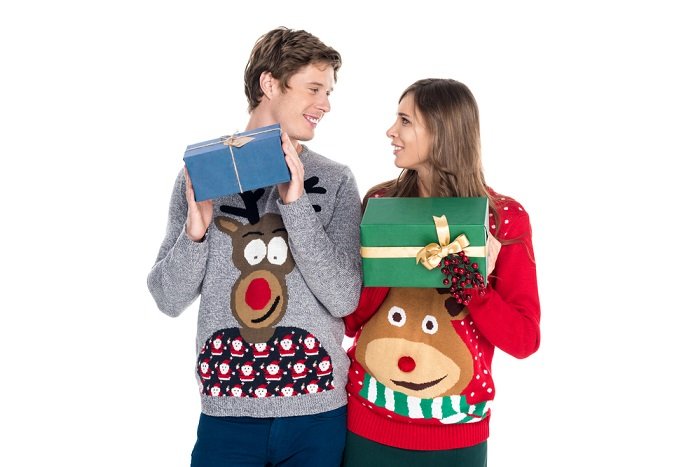 Christmas couple photoshoot tips: a couple in Christmas sweaters holding each others Christmas gifts