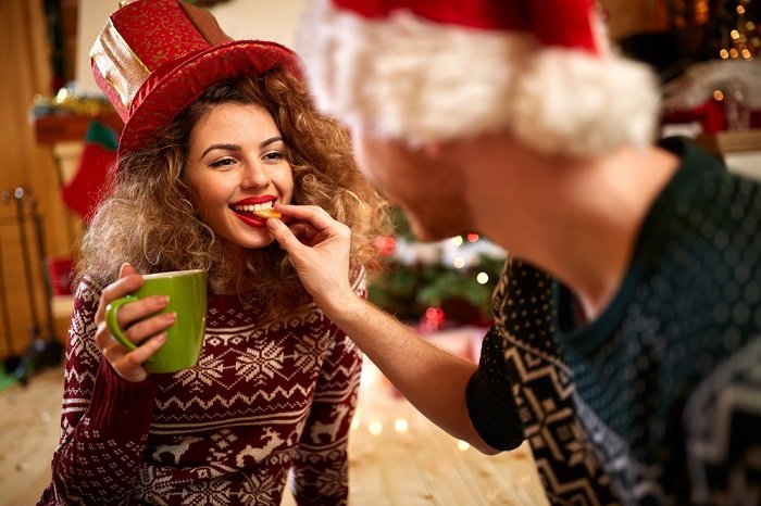 christmas couple photoshoot ideas: a man feeding his girlfriend a cookie 