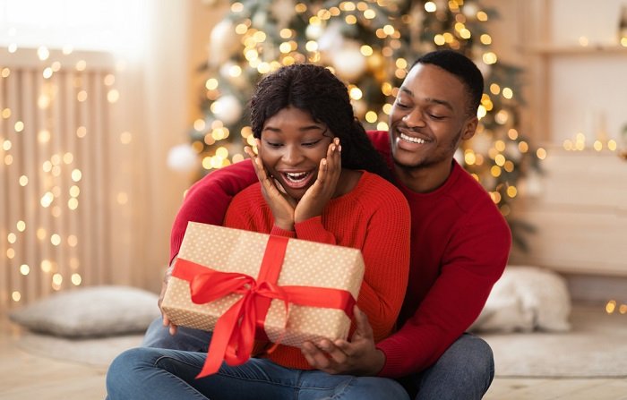 Christmas couple photoshoot ideas: a boyfriend presents his girlfriend with a Christmas present 