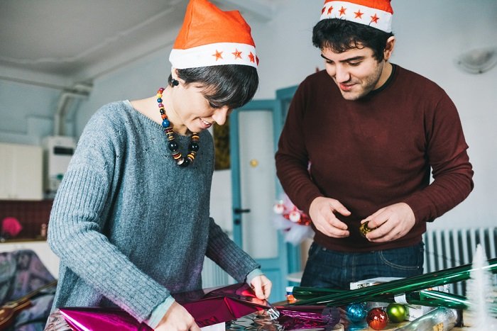 Christmas couple photoshoot tips: a couple in Santa hats wrap Christmas presents together