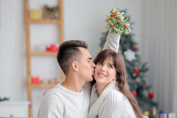 Tips for a Christmas couple photoshoot: a guy giving his girlfriend a kiss in the cheek under the mistletoe 