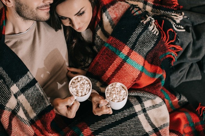 Christmas couple photoshoot tips: a couple cozies up next to each other to drink their hot chocolate