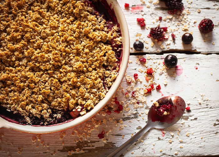 A berry crumble in a bowl agains a wood food photography prop background