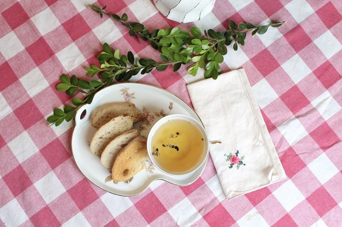 Tea in a cup and bread on a plate on top of a gingham food photography prop tablecloth