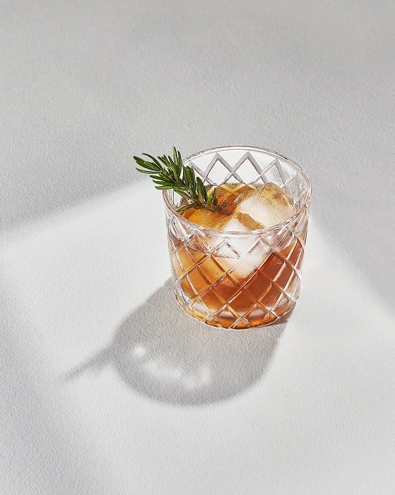 An alcoholic drink with ice and rosemary in a glass tumbler used as a food photography props