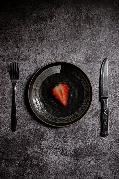 A sliced strawberry on a black plate and with a fork and knife used as food photography props