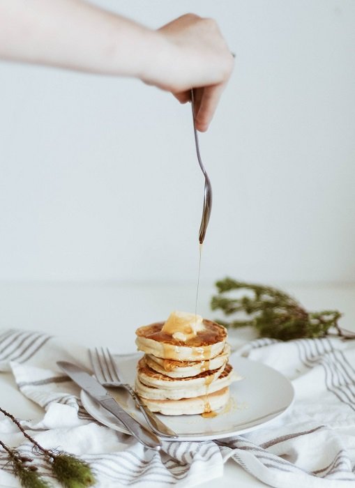 Food Photography tips: someone out of frame drizzles honey off of a spoon and onto a stack of pancakes