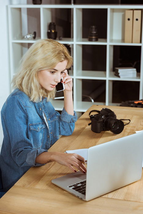 a woman talking on her cell phone while looking at her laptop