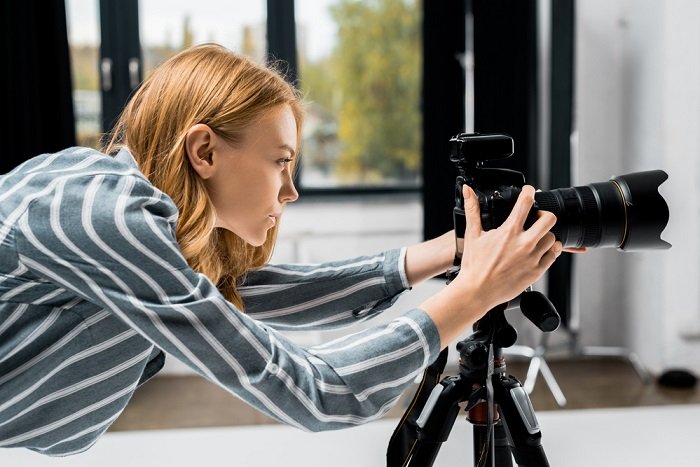 a photographer looking at the settings of her camera mounted on a tripod