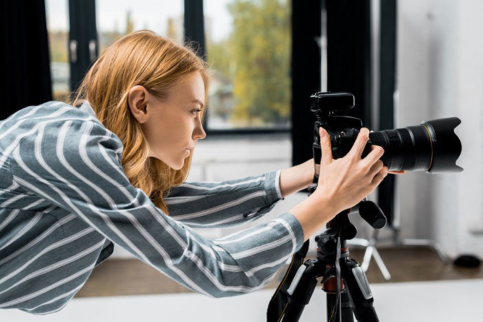 a photographer looking at the settings of her camera mounted on a tripod