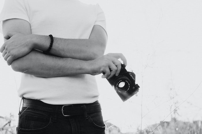 Torso of a photographer wearing a white t-shirt and holding a camera