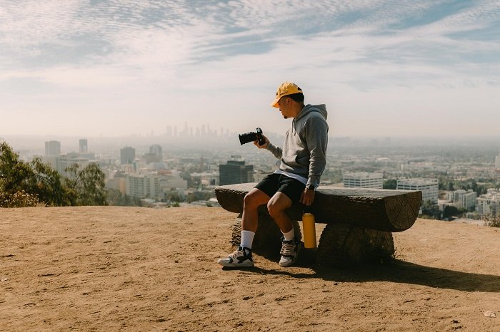 a photographer sits on a bench overlooking the skyline of a city 