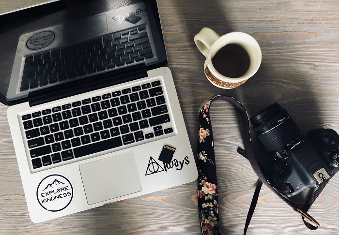 a flat lay photo of a laptop, camera, and cup of coffee