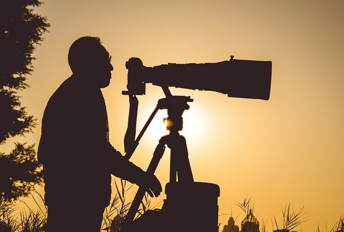 Silhouette of a photographer with a camera and large telephoto lens on a tripod