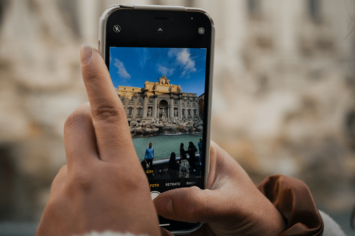 A close-up of hands holding a camera phone with the native app open taking a travel photo