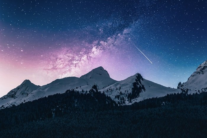 a purple and blue tinted image of a galaxy above mountains using an ND astrophotography filter
