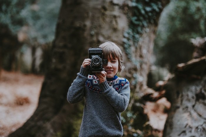 a young boy taking a photo in the woods