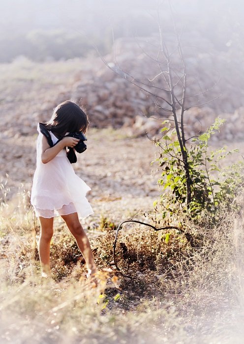 a young girl takes a photo of a bush in a field 