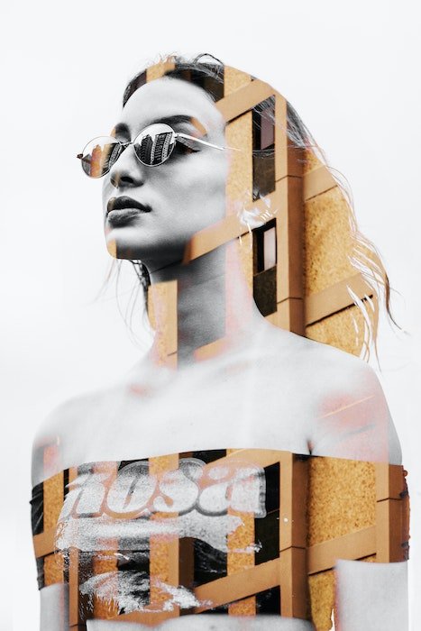 Double exposure of a girl and a tall building. Model is wearing glasses and is a black and white image whereas the building is in color.