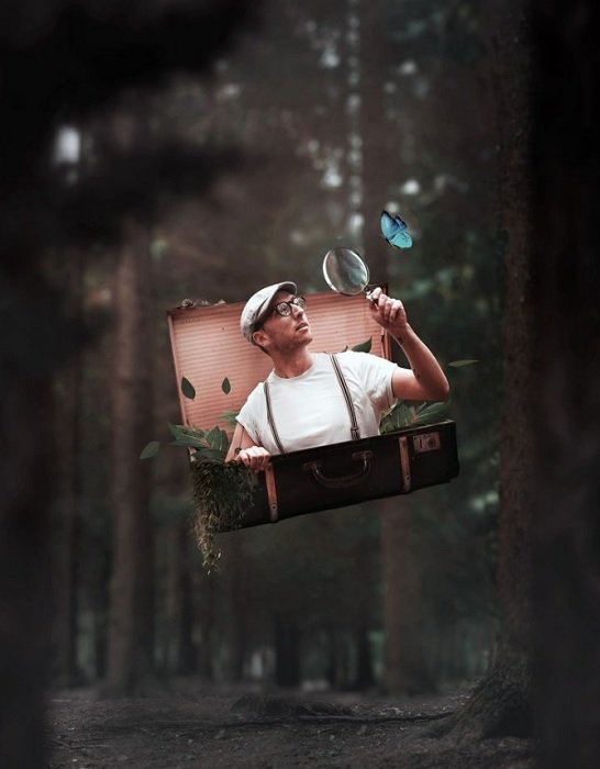 Photo manipulation idea of a man holding a magnifying glass coming out of suitcase in woods