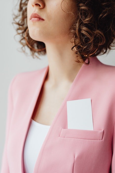 Business cards in top pocket of woman who is wearing a pink jacket. 