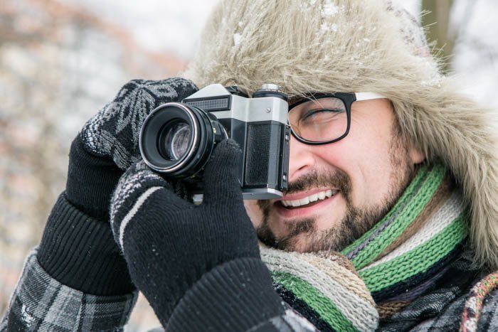 Man wearing winter photography gloves and hat taking a picture with a camera