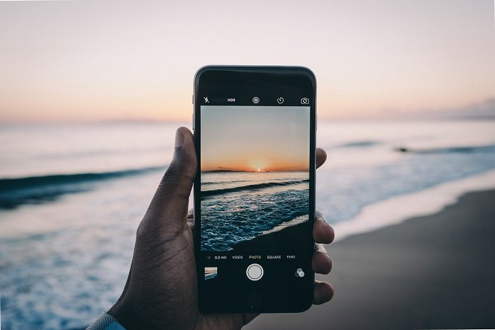 a man's hand holding a smartphone with a sunset frame