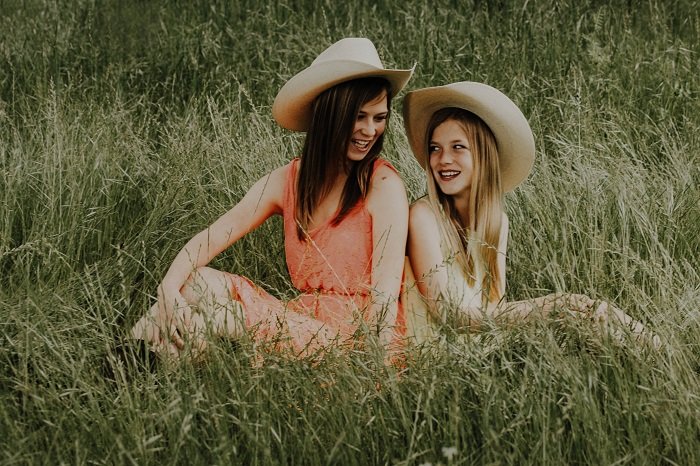 Two girls in cowboy hats sitting in a field a sisters photoshoot idea