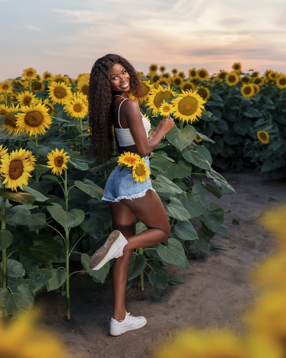 Model with leg up posing amongst sunflowers with flowers in her hands and in her pockets 