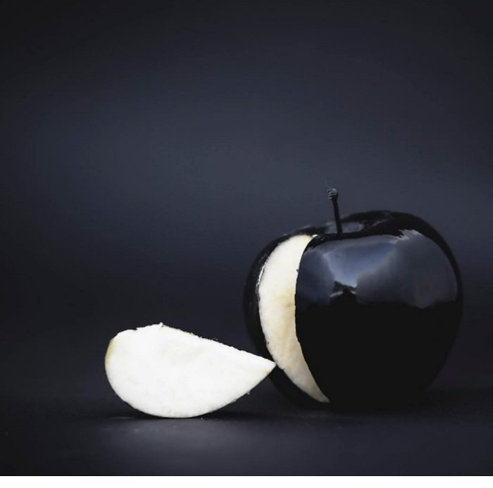 an image of a black apple with a slice cut out against a black background as a surreal photography example