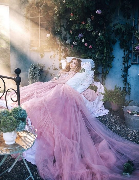Woman in pink dress on bed in a garden as an example of fairy tale photography