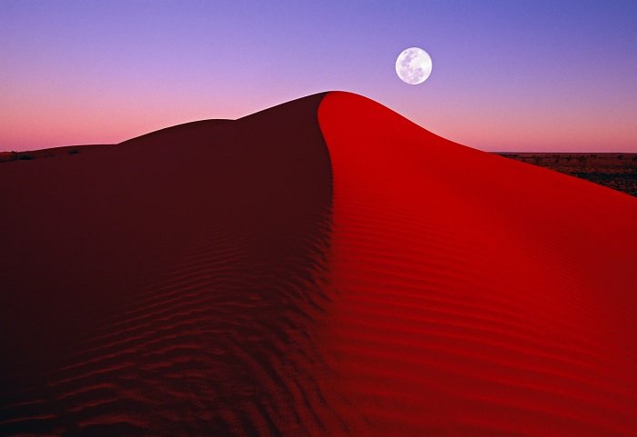 Sand dune with moon in the background at dusk
