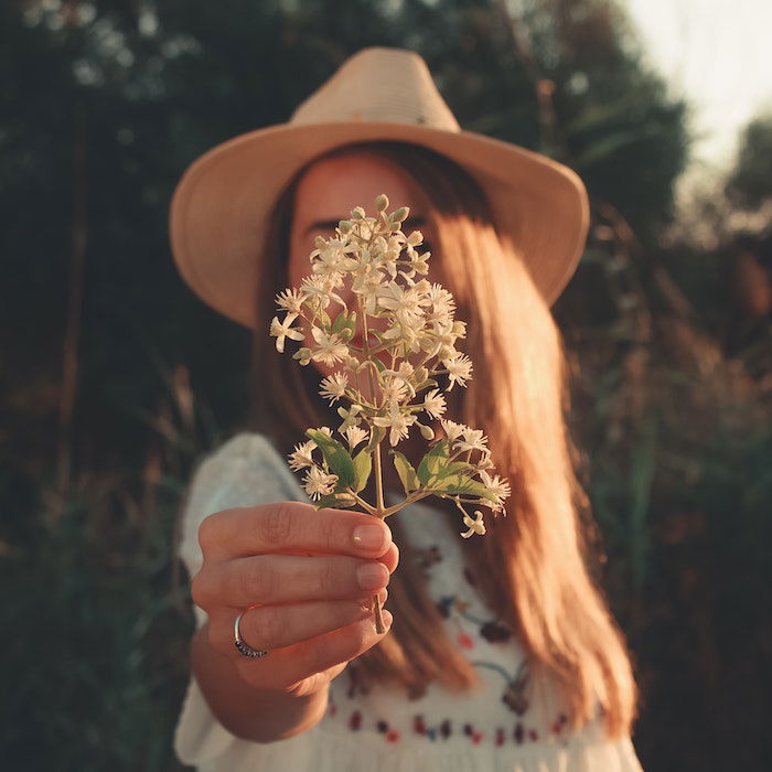 Portrait of a woman in hat holding wildflowers up to the camera to hide her face