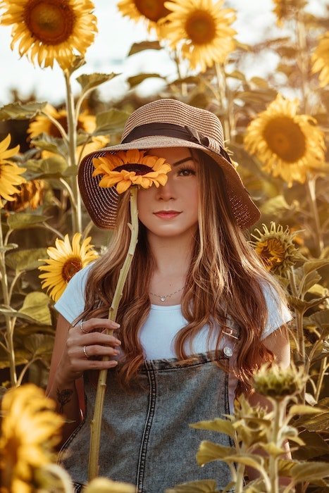 Woman's portrait in a sunflower field holding one up to cover her eye