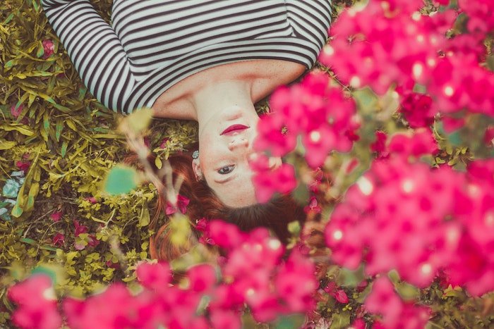 An overhead portrait of a woman lying down on the ground with flowers in the foreground