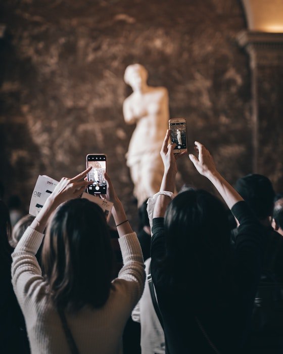 People taking pictures of a sculpture in the background with smartphones