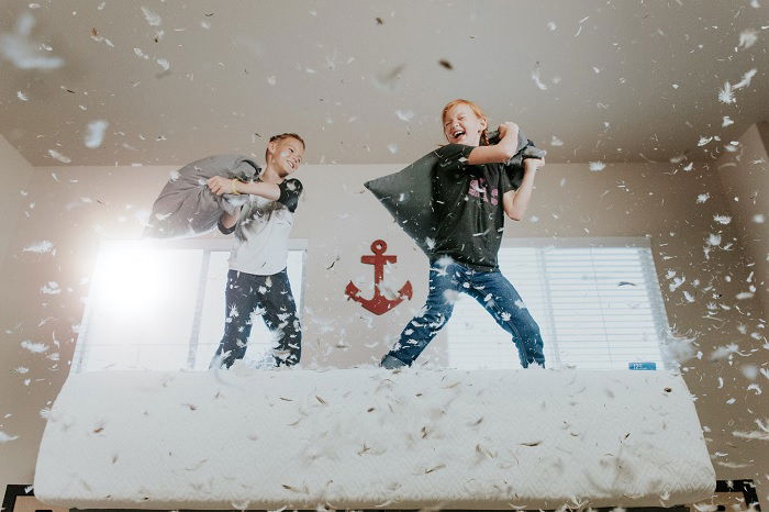 Two boys fighting with pillows on a bed