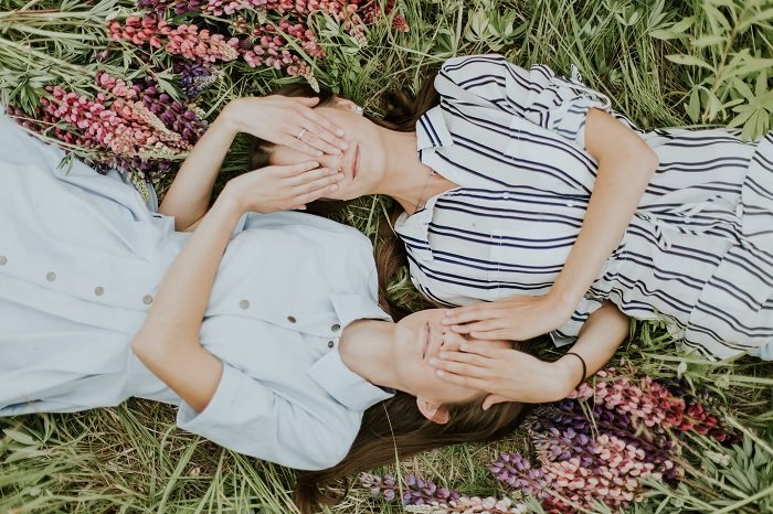 Two girls lying in a field covering each others eyes