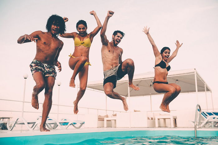 Four young adults jumping into a simming pool