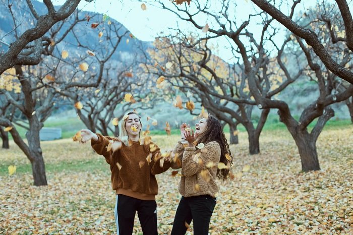 Two women throwing autumn leaves in the air