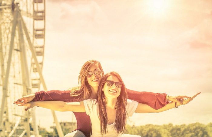 Two female friends in front of a ferriswheel doing the titanic pose as an example of a fun best friend photoshoot
