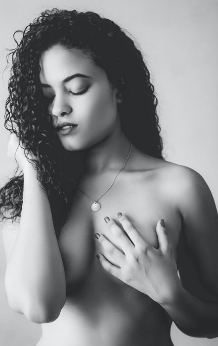 Topless woman with curly hair covering chest with arms as a boudoir pose